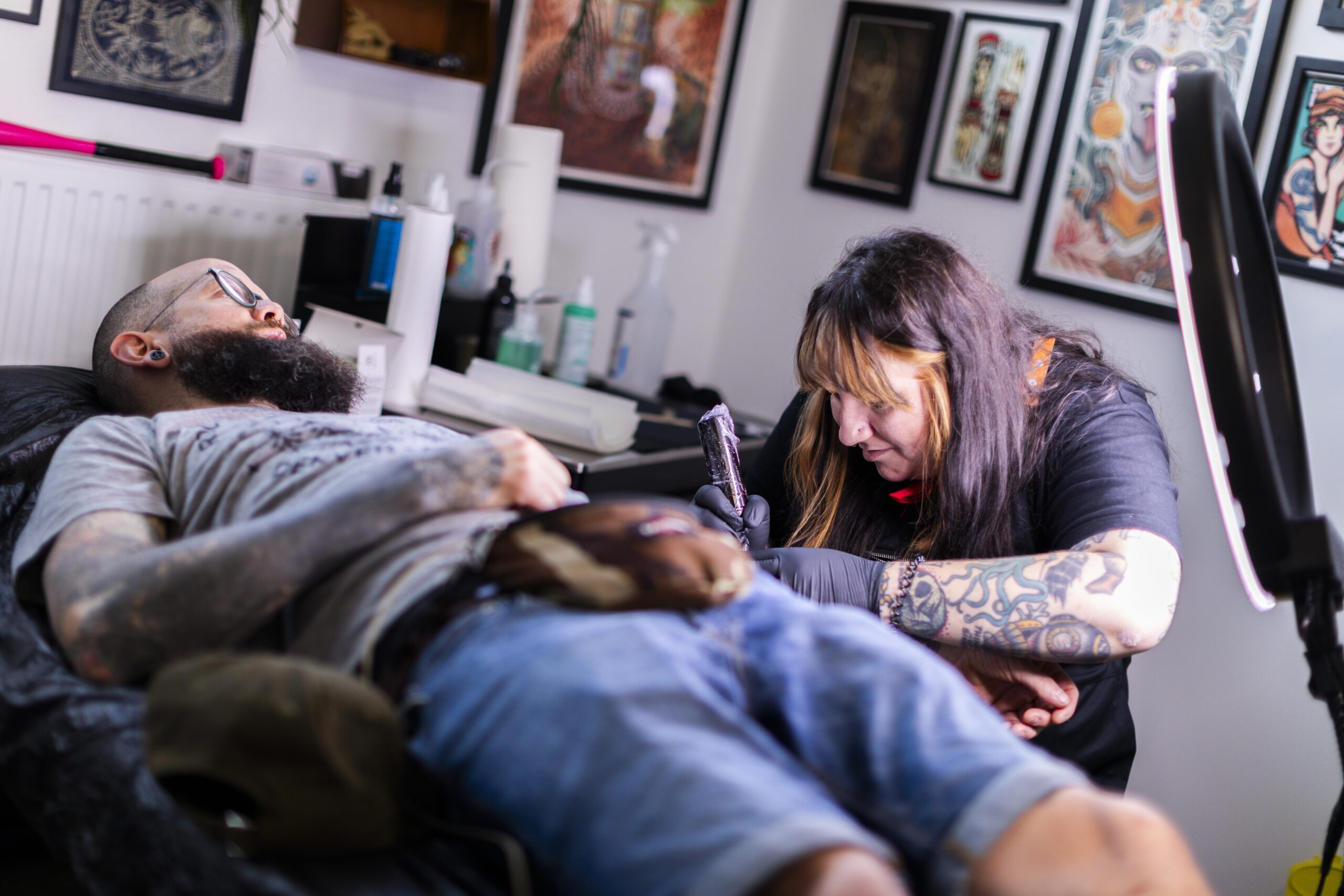 Im Bild eine Tätowiererin mit einem Kunden im Happy Dragon Tattoo Studio in der Tabakfabrik Linz. Sie tätowiert ihn, auf der Liege liegend.