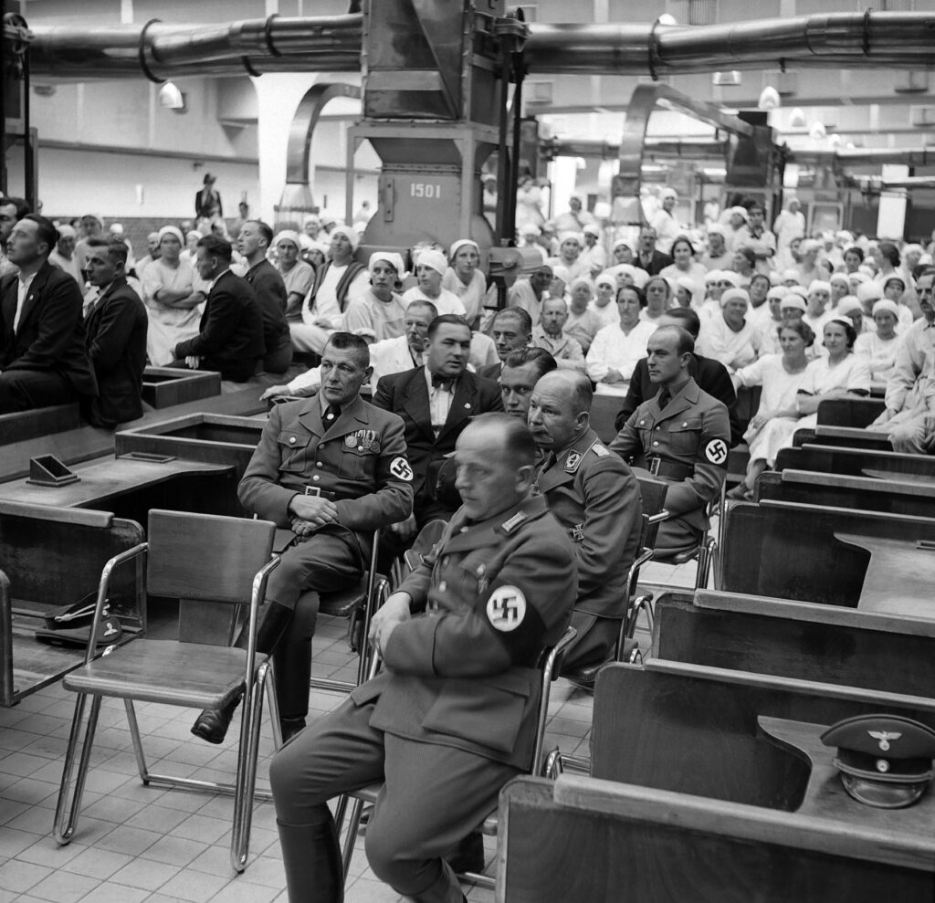 Nationalsozialisten in Uniform und Arbeiter:innen der Tabakfabrik bei einem Werkskonzert 1938.