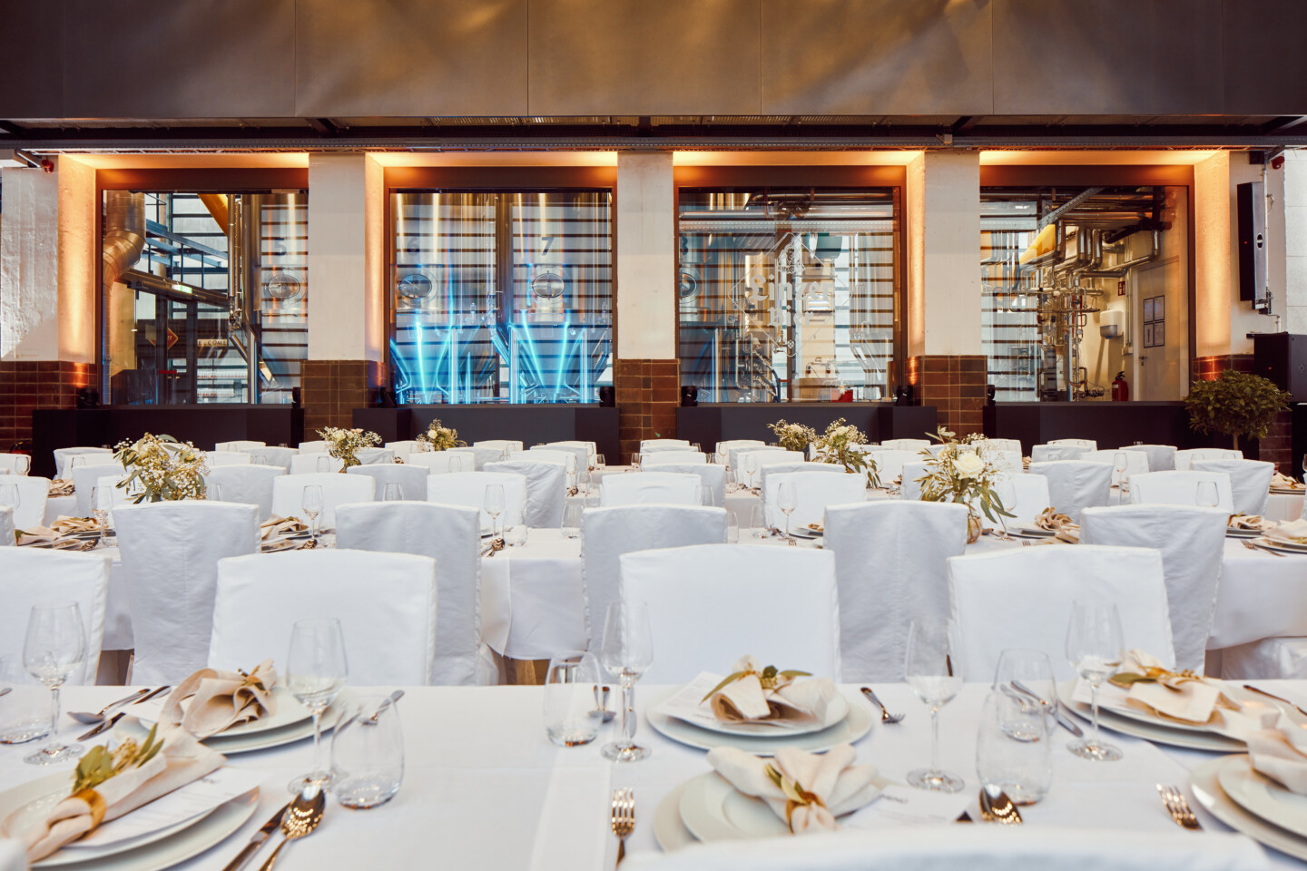 Hochzeitssetting im Hörsaal, Bestuhlung in Bankett mit weißen Tischtüchern, Deko und Blick auf die Biertanks.