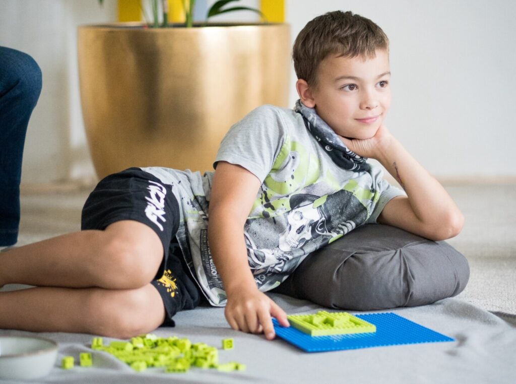 Ein Bub liegt am Boden, hat Lego gebaut und hört aufmerksam zu. Sommerprogramm Innerversum.