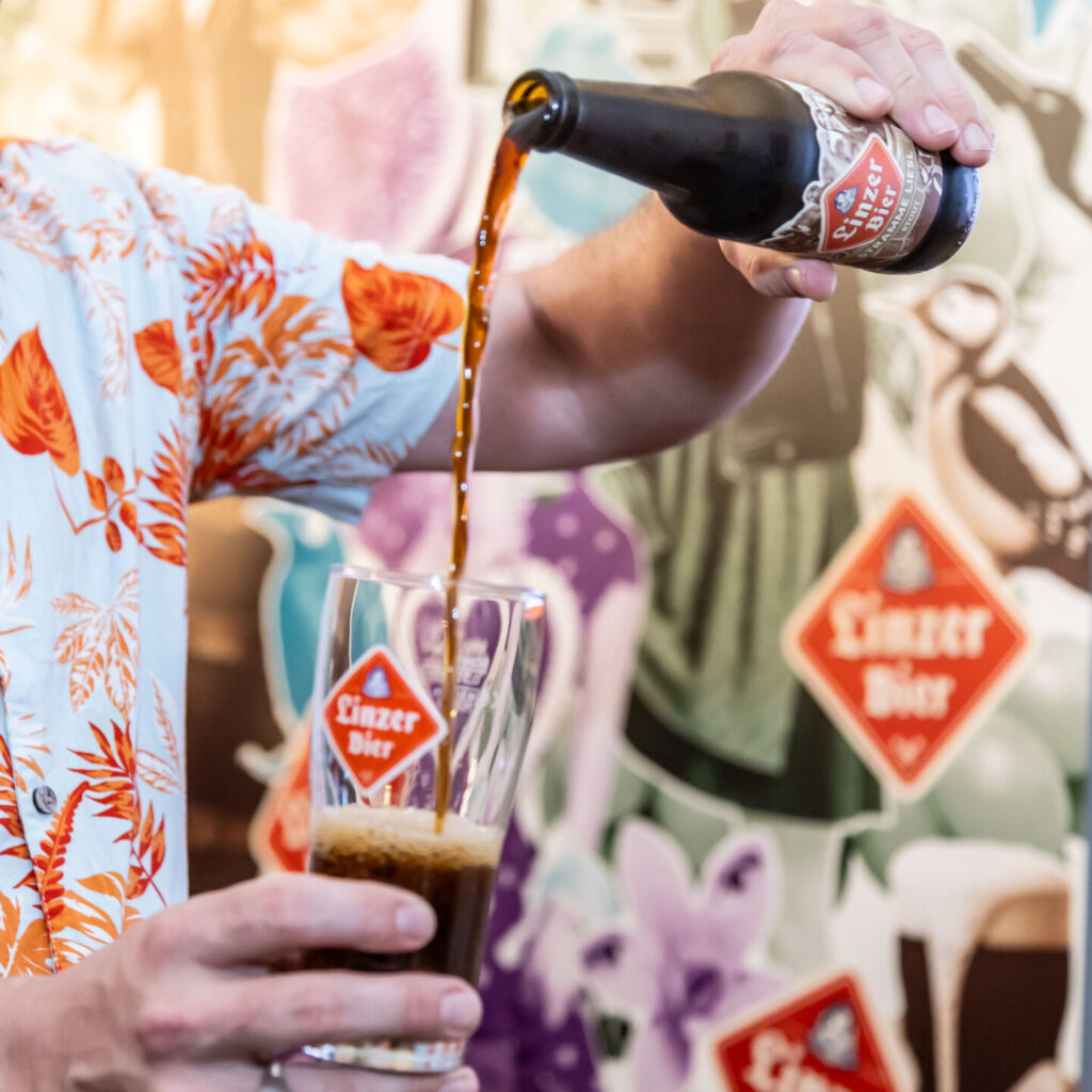 Anschnitt eines Bilder, wo nur die Hände, ein Glas und eine Flasche Linzer Bier zu sehen sind. Es wird Bier eingeschenkt.
